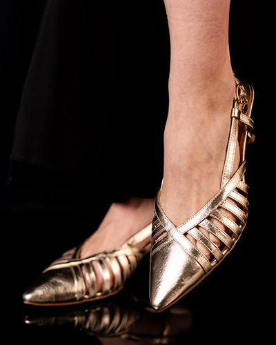 A woman's foot wearing a black ankle strap heel called PAYTEN with intricate rhinestones and gold embroidery